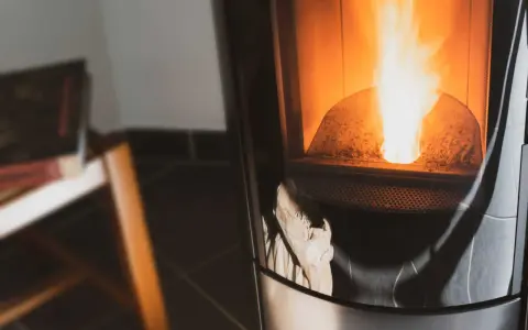Flammes vives dans un poêle à granulés couleur cendre. Un sac en papier est visible en bas, prêt à être utilisé.