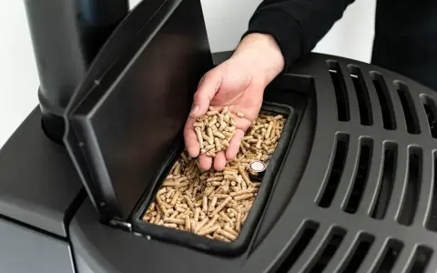 Main d'homme versant des granulés de bois dans un poêle, signalant une alarme manque pellet.