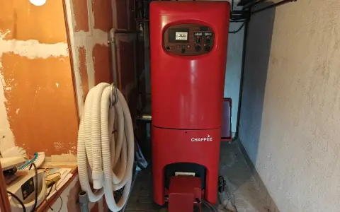 Chaudière rouge Chappée dans une pièce. Un tuyau blanc enroulé est accroché au mur. Pensez à l'assurance chaudière pour votre confort.
