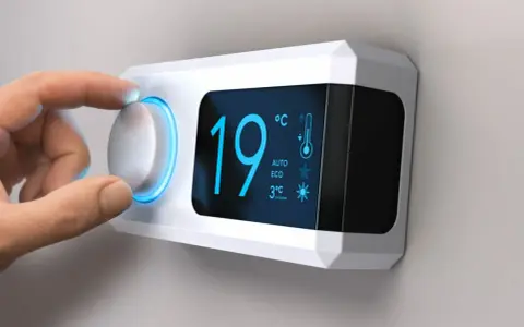 Main d'une personne ajustant le réglage de température sur un cee thermostat connecté affichant 19°C.