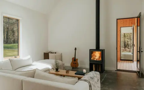 Salon cosy avec poêle à bois allumé, guitare et canapé. Une aide financière pour le tubage de cheminée pourrait rendre ce lieu encore plus chaleureux.
