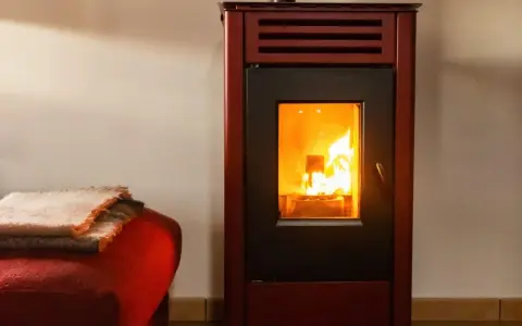 Poêle à bois avec soufflerie, ses flammes dansent joyeusement, réchauffant la pièce. Une couverture douillette est posée sur un fauteuil rouge à proximité.