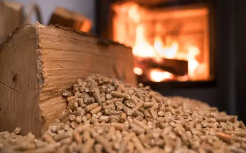 Bûches et granulés de bois, prêts pour une chaudière bois mixte. Le feu crépite en arrière-plan.