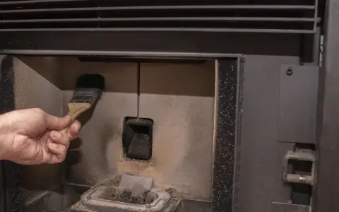 Main d'une personne nettoyant la chambre de combustion d'un poêle à pellet MCZ avec une brosse. Un problème de nettoyage peut causer des dysfonctionnements.