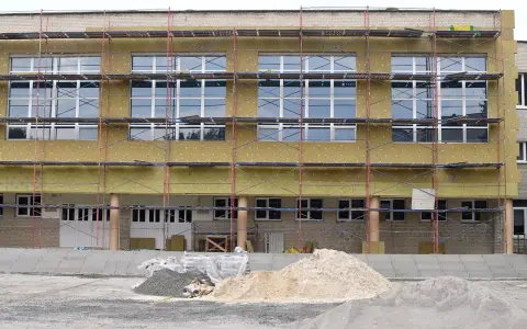 Bâtiment en rénovation énergétique, échafaudages et isolation jaune recouvrent la façade. Des tas de sable et de gravier sont prêts pour les travaux.