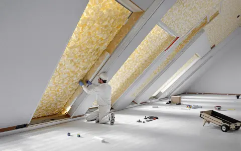 Un ouvrier installe un isolant thermique jaune texturé dans un grenier.