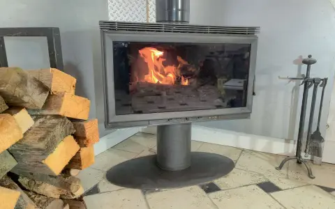 Un poêle à bois avec une vitre propre pour changer une vitre de poele a bois. Des bûches de bois sont empilées à gauche.