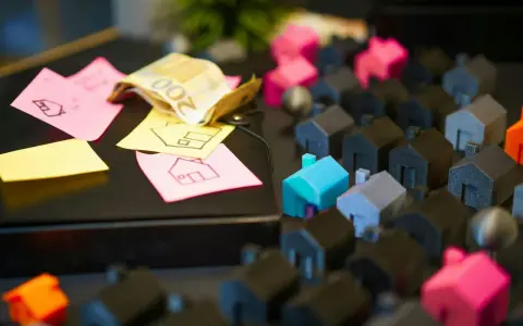 Petites maisons miniatures, billets de banque et post-its avec des dessins de maisons.