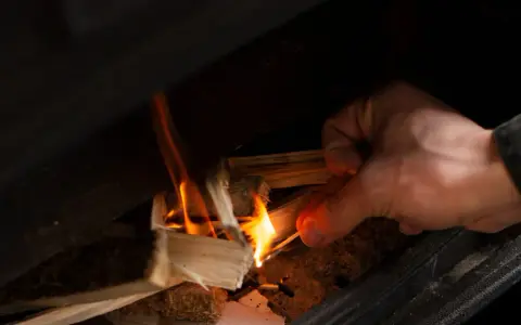 Main allumant un feu dans un poêle à bois avec une allumette.