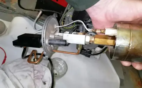 Main d'un technicien ajustant un composant de chaudière fioul en sécurité. Tuyaux en cuivre et raccords laiton visibles.