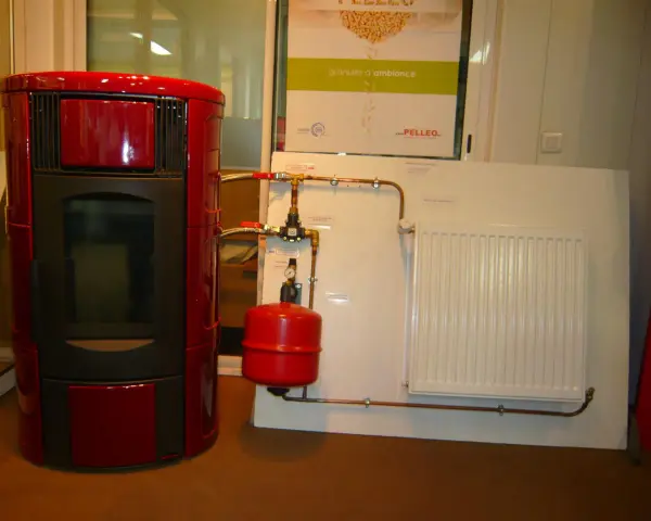 Poêle à granulé hydro rouge connecté à un radiateur blanc. Le système de chauffage est prêt.