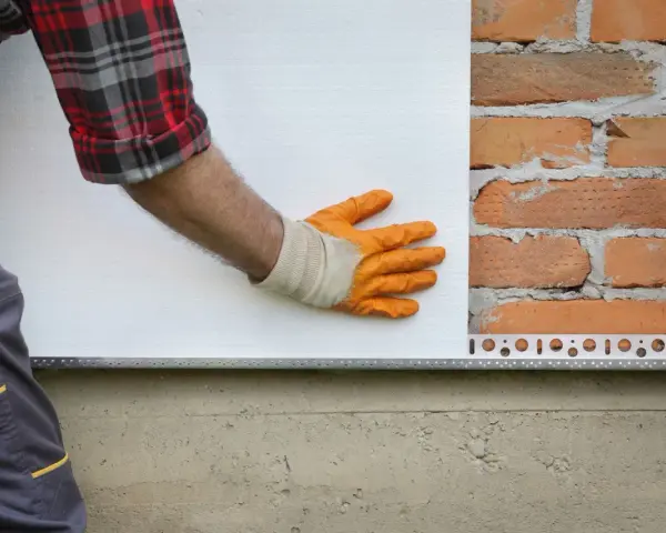 Pose d'isolant blanc sur mur de briques. Estimation du prix isolation extérieur maison 140m2.