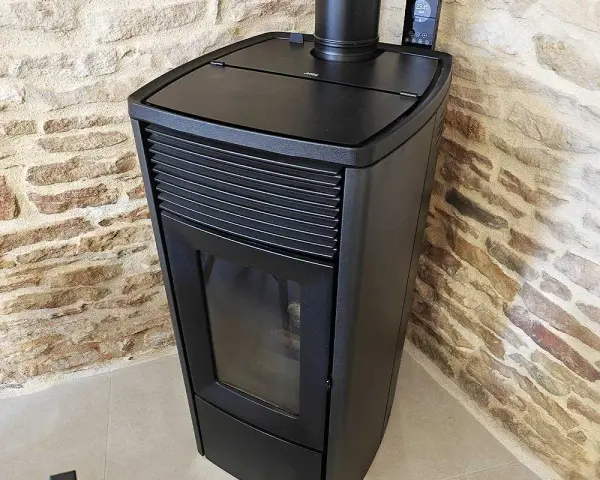 Poêle à granulés noir moderne, avec écran de contrôle, adossé à un mur de pierres. Apprenez comment éteindre un poêle à granulé en toute sécurité.