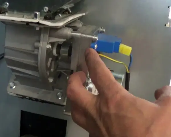 Main d'un homme manipulant le mécanisme d'un poêle à granulés, pour nettoyer le pressostat.