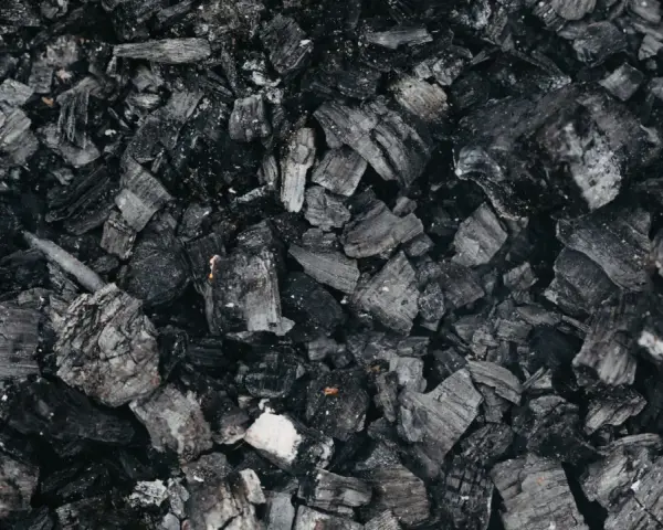 Gros plan sur des morceaux de machefer pellet, résidus noirs et gris de combustion, évoquant la chaleur d'un feu de bois.