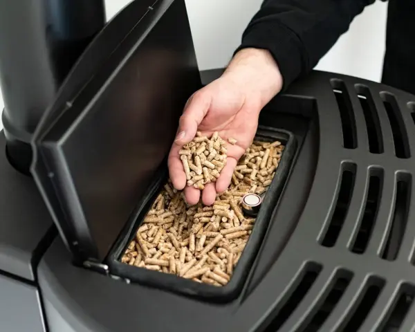 Main d'homme versant des granulés de bois dans un poêle, signalant une alarme manque pellet.