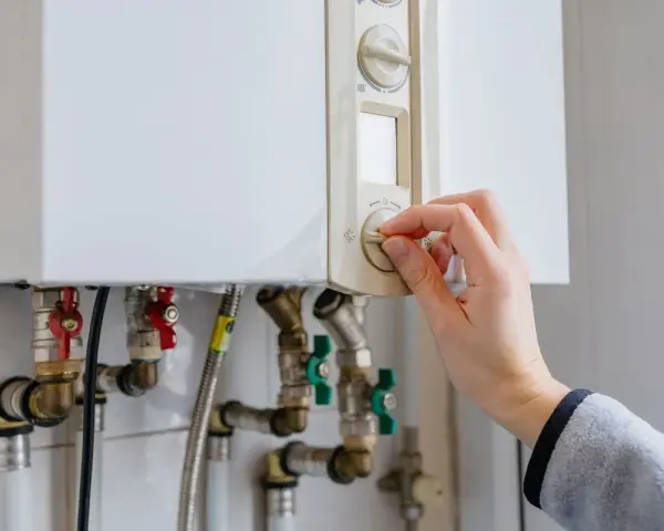 Main tenant ajuste le thermostat de sa chaudière à gaz. Une aide pour le changement de chaudière gaz est peut-être nécessaire.
