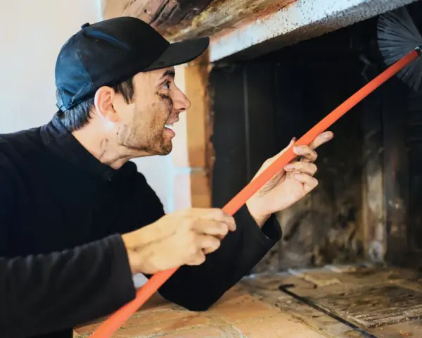 Ramoneur au visage barbouillé de suie utilise une brosse pour nettoyer le conduit d'un poêle à bois, assurant le bon fonctionnement du deflecteur poele a bois.