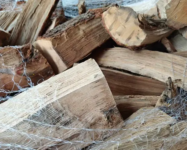 Gros tas de bois humide, prêt pour le poêle. Les bûches sont emballées dans un filet blanc.