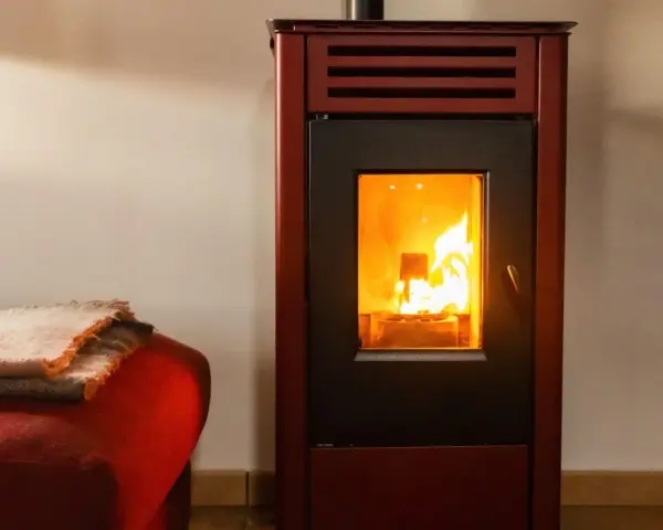 Poêle à bois avec soufflerie, ses flammes dansent joyeusement, réchauffant la pièce. Une couverture douillette est posée sur un fauteuil rouge à proximité.