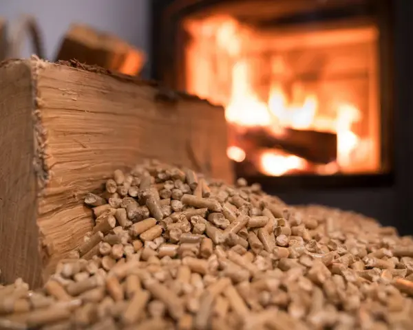 Bûches et granulés de bois, prêts pour une chaudière bois mixte. Le feu crépite en arrière-plan.