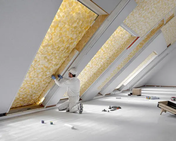 Un ouvrier installe un isolant thermique jaune texturé dans un grenier.