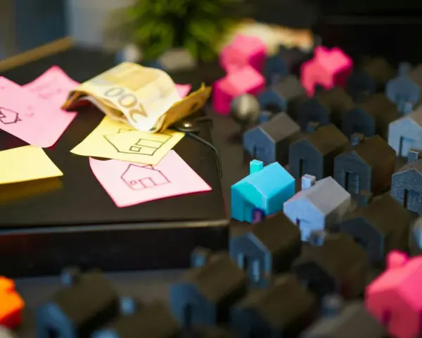 Petites maisons miniatures, billets de banque et post-its avec des dessins de maisons.