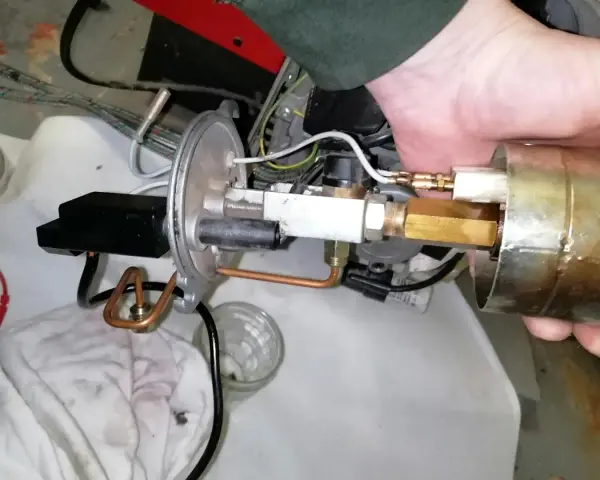 Main d'un technicien ajustant un composant de chaudière fioul en sécurité. Tuyaux en cuivre et raccords laiton visibles.