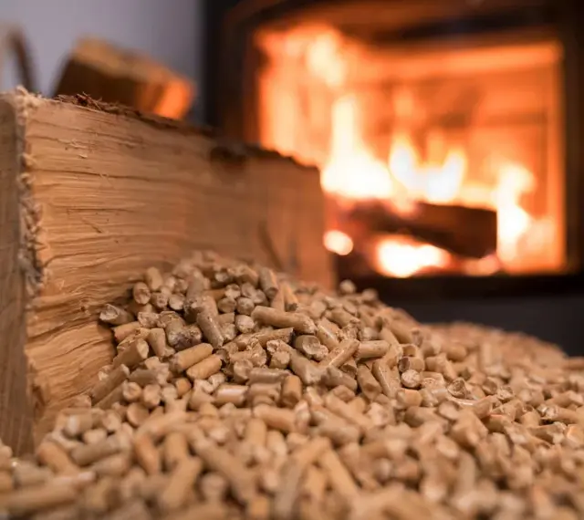 Bûches et granulés de bois, prêts pour une chaudière bois mixte. Le feu crépite en arrière-plan.