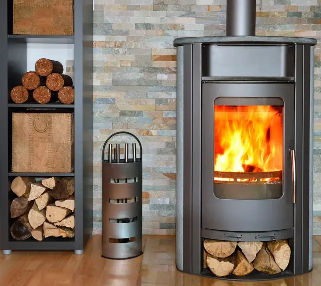 Poêle moderne avec un feu vif, entouré de bois de chauffage et de pellets rangés dans une étagère.