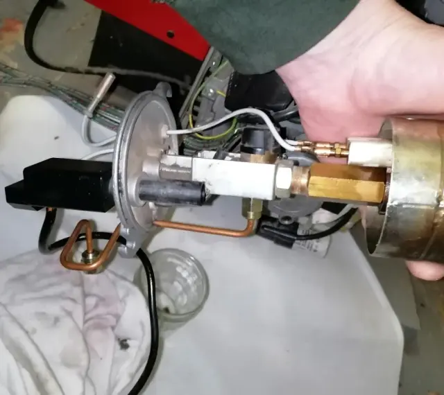 Main d'un technicien ajustant un composant de chaudière fioul en sécurité. Tuyaux en cuivre et raccords laiton visibles.