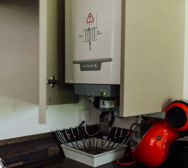 Chaudière gaz instantané De Dietrich installée dans un placard, à côté d'une machine à café rouge.
