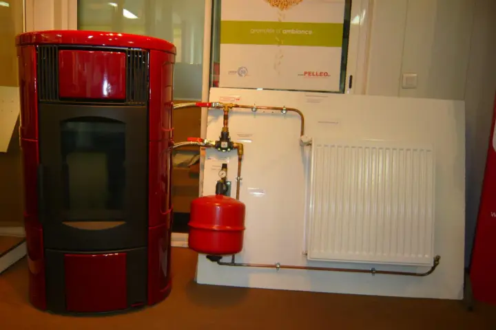 Poêle à granulé hydro rouge connecté à un radiateur blanc. Le système de chauffage est prêt.