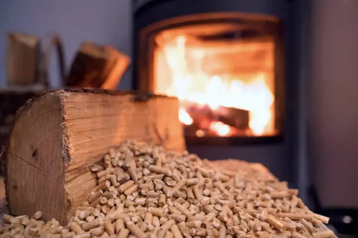 Un poêle à bois Prime Renov crache des flammes chaleureuses. Devant, une bûche et des granulés de bois attendent d'être utilisés.