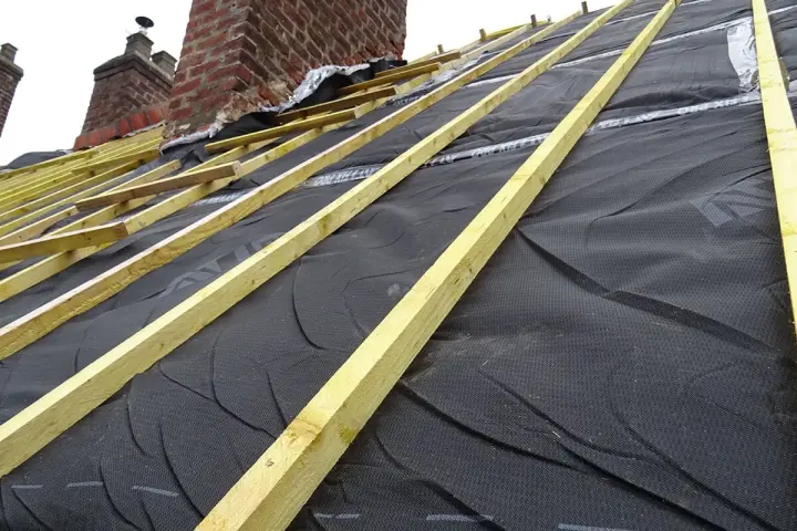 Charpente de toiture avec isolant noir et liteaux en bois, près de cheminées en brique.