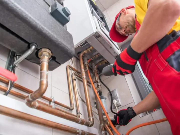 Un technicien installe une chaudière à gaz, une étape clé pour ma prime rénov. Il manipule des tuyaux en cuivre avec soin.