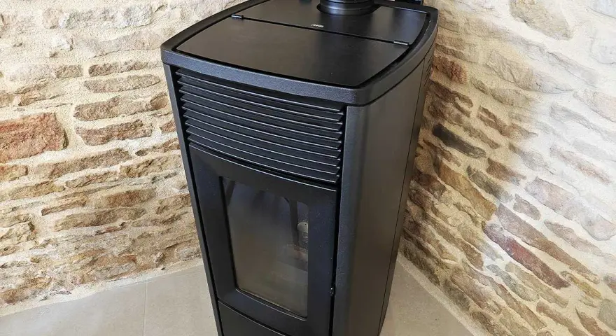 Poêle à granulés noir moderne, avec écran de contrôle, adossé à un mur de pierres. Apprenez comment éteindre un poêle à granulé en toute sécurité.