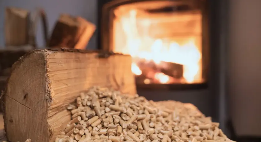 Un tronc de bois et des granulés attendent le tirage poêle à bois. Le feu crépite dans le foyer en arrière-plan.