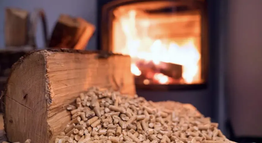 Un poêle à bois Prime Renov crache des flammes chaleureuses. Devant, une bûche et des granulés de bois attendent d'être utilisés.
