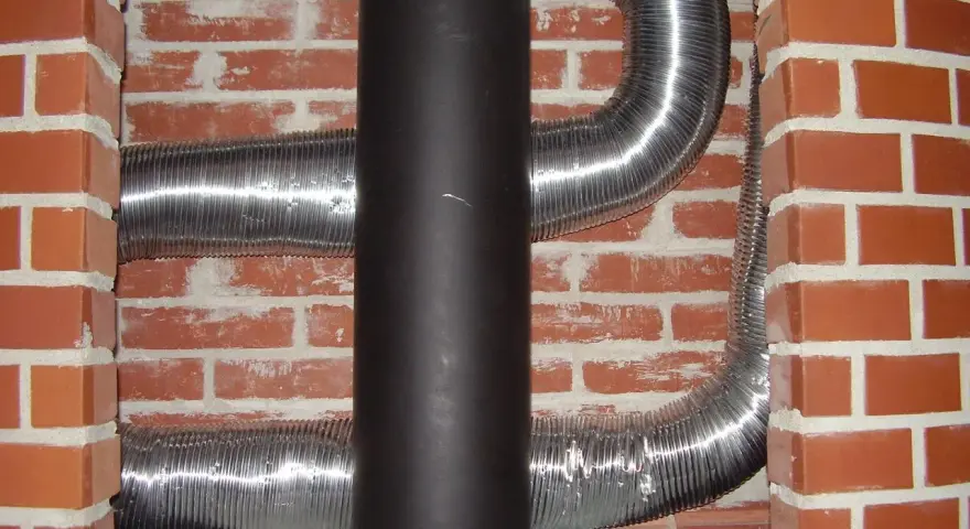 Mur brique réfractaire derrière poêle, avec conduits métalliques flexibles.