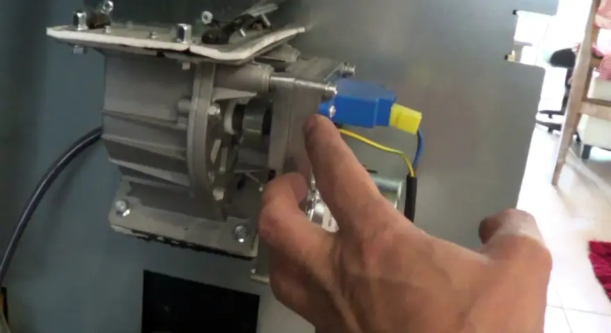 Main d'un homme manipulant le mécanisme d'un poêle à granulés, pour nettoyer le pressostat.