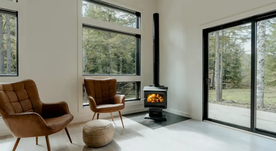 Un poêle à granule appartement, avec deux fauteuils en cuir marron et une vue sur la forêt.
