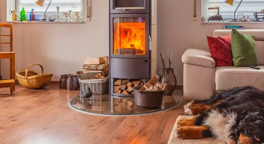 Poêle à bois allumé, bois empilé, canapé et chien endormi dans un salon confortable.