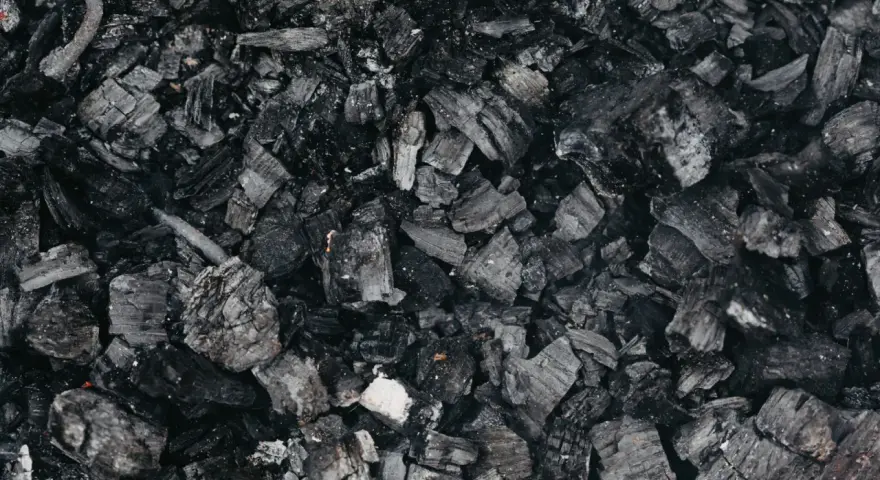 Gros plan sur des morceaux de machefer pellet, résidus noirs et gris de combustion, évoquant la chaleur d'un feu de bois.