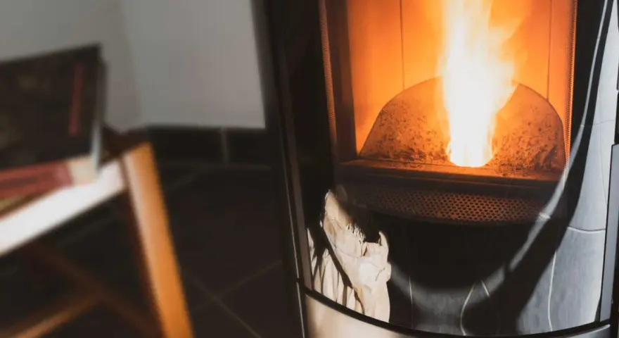 Flammes vives dans un poêle à granulés couleur cendre. Un sac en papier est visible en bas, prêt à être utilisé.