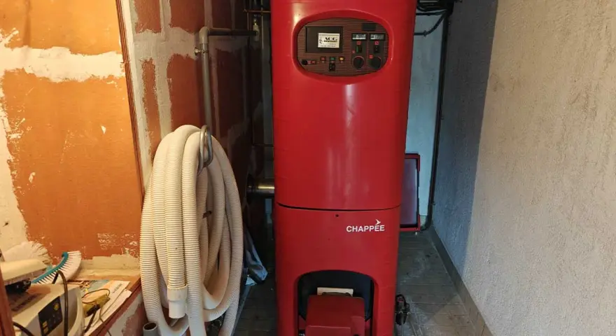 Chaudière rouge Chappée dans une pièce. Un tuyau blanc enroulé est accroché au mur. Pensez à l'assurance chaudière pour votre confort.