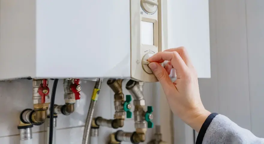Main tenant ajuste le thermostat de sa chaudière à gaz. Une aide pour le changement de chaudière gaz est peut-être nécessaire.