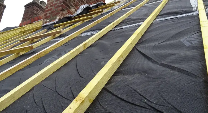 Charpente de toiture avec isolant noir et liteaux en bois, près de cheminées en brique.