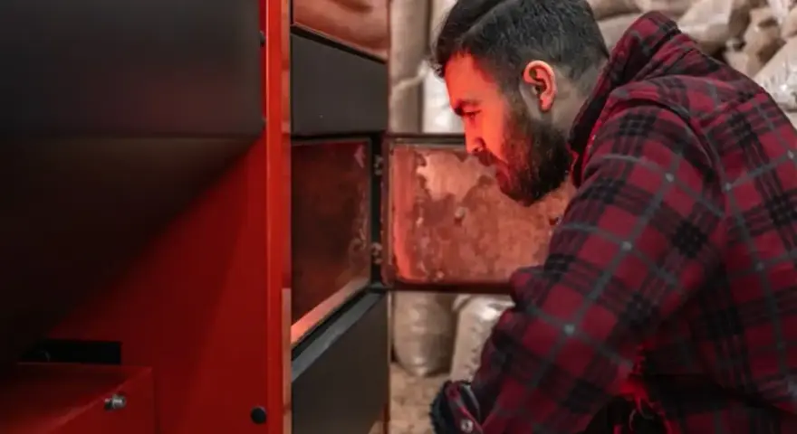 Homme vérifiant un poêle à granulés, peut-être une alarme 6 s'est déclenchée. Sacs de granulés en arrière-plan.