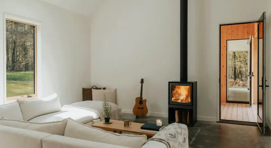 Salon cosy avec poêle à bois allumé, guitare et canapé. Une aide financière pour le tubage de cheminée pourrait rendre ce lieu encore plus chaleureux.